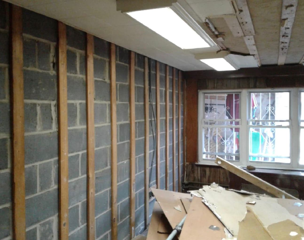 Wooden studs attached to a cinder block wall in a room under renovation with debris.