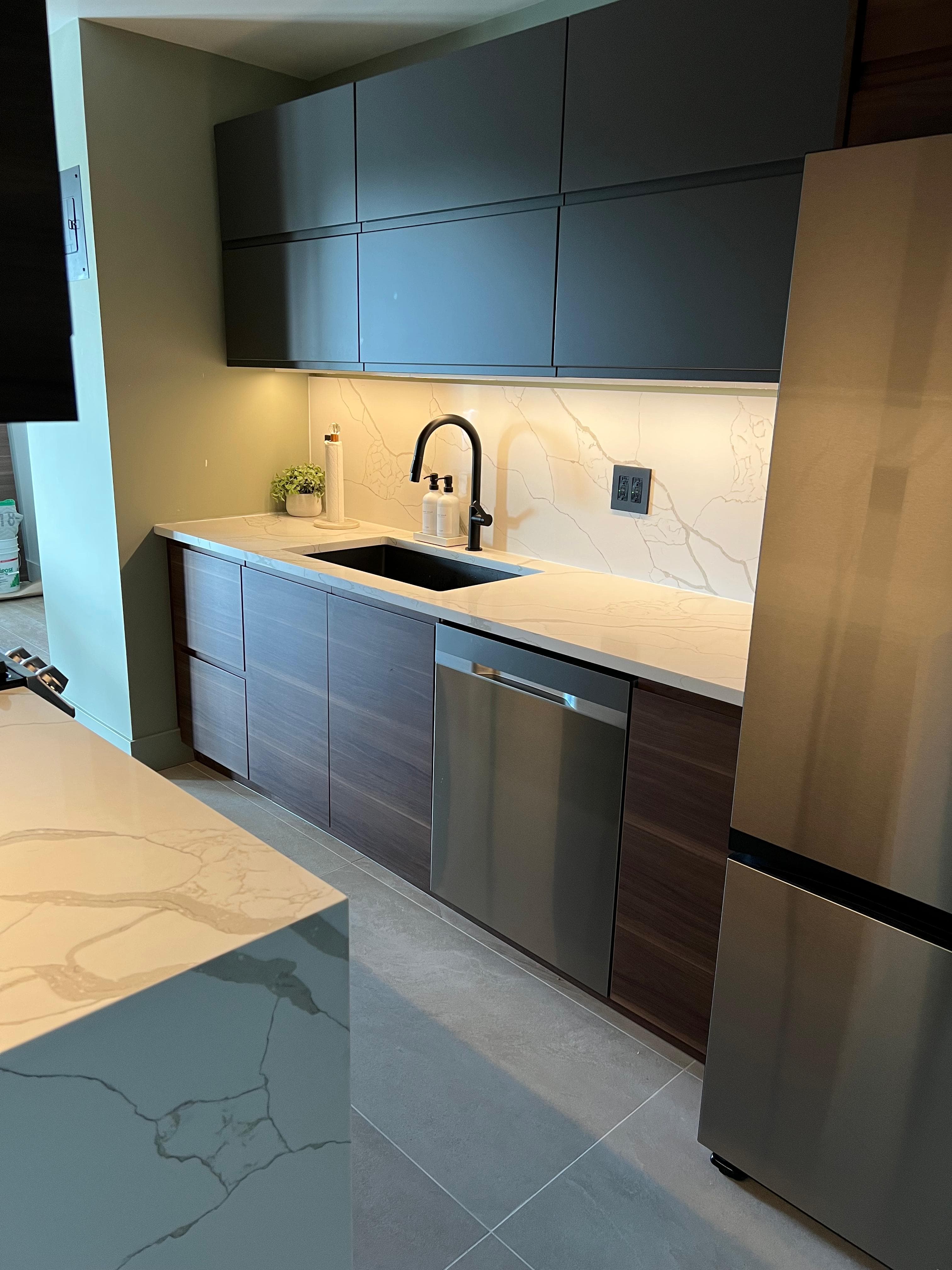 Modern kitchen with dark grey upper cabinets, wood lower cabinets, marble countertops, and stainless steel appliances.