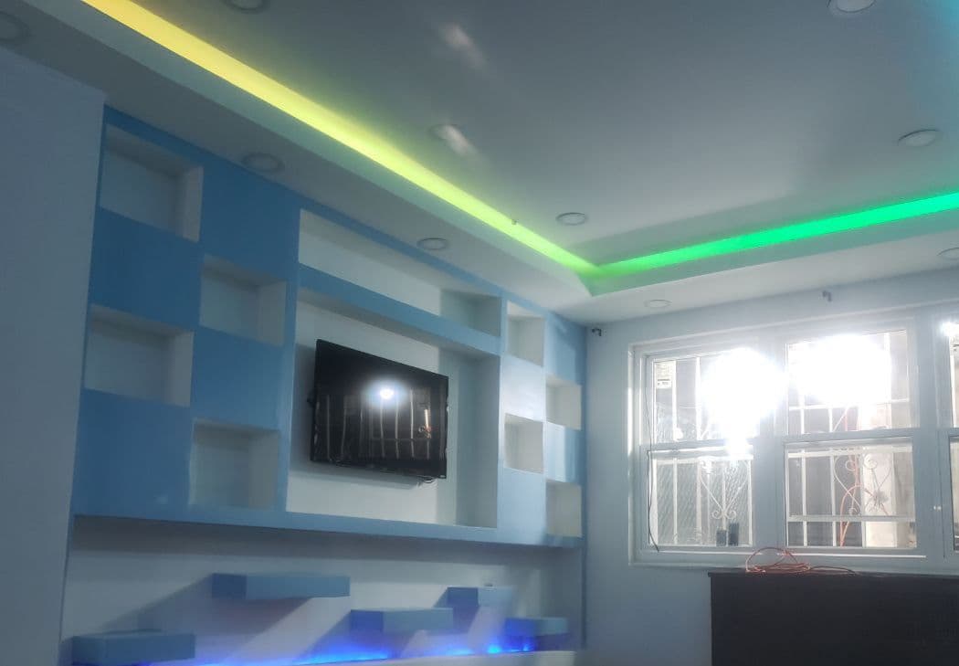 Modern blue and white geometric wall unit with mounted TV and colorful LED ceiling lights.